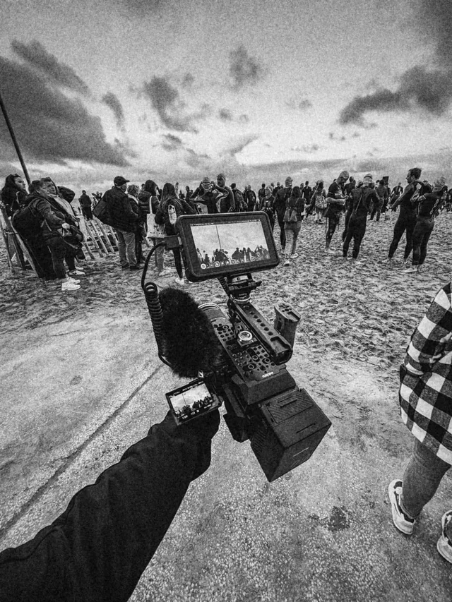 Caméra au poing sur la plage, au milieu des triathlètes en combinaison avant le départ
