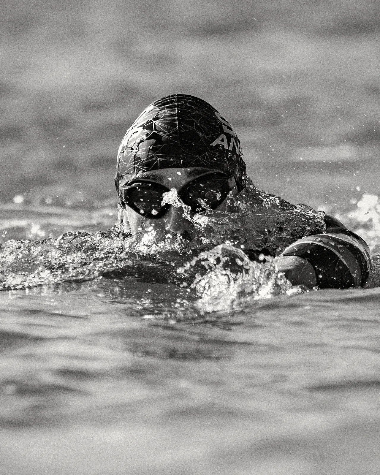 Triathlète nageant en eau libre avec des lunettes Enihcam à verres teintés, en noir et blanc