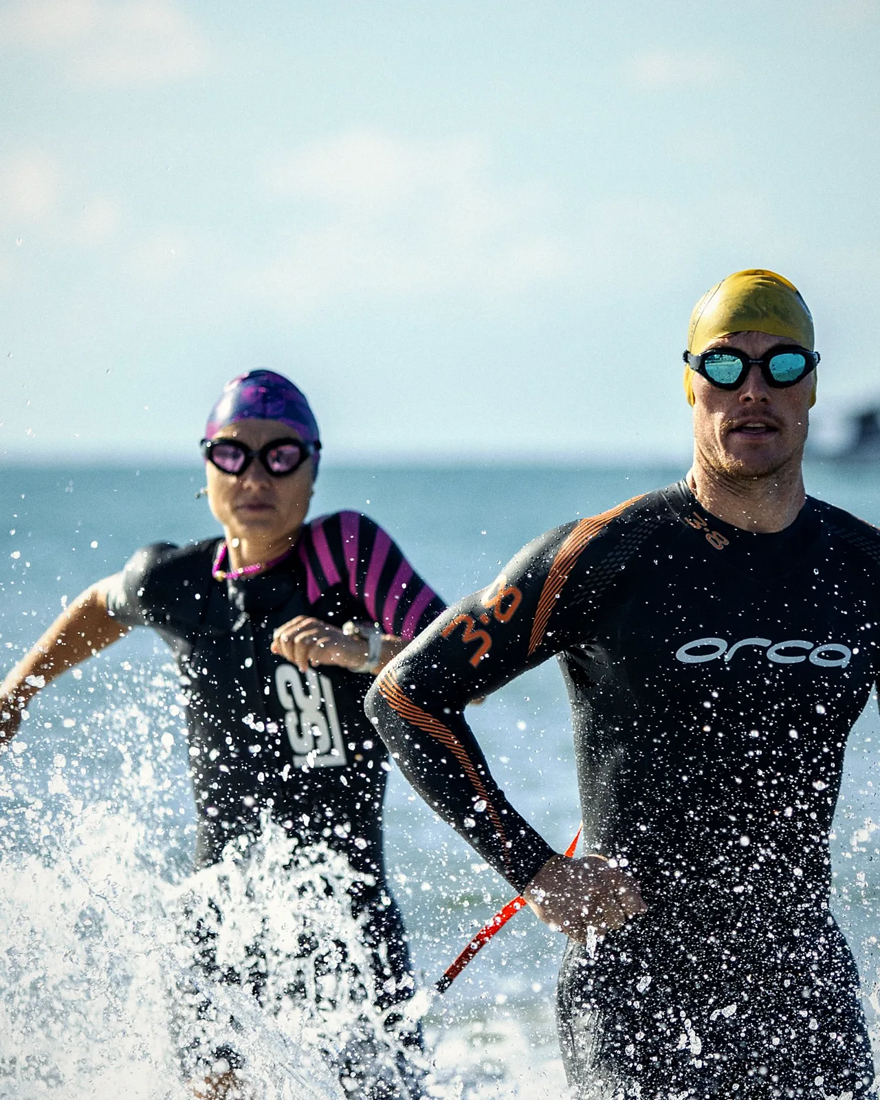 Deux triathlètes en combinaison sortent de la mer en courant, éclaboussures autour d’eux