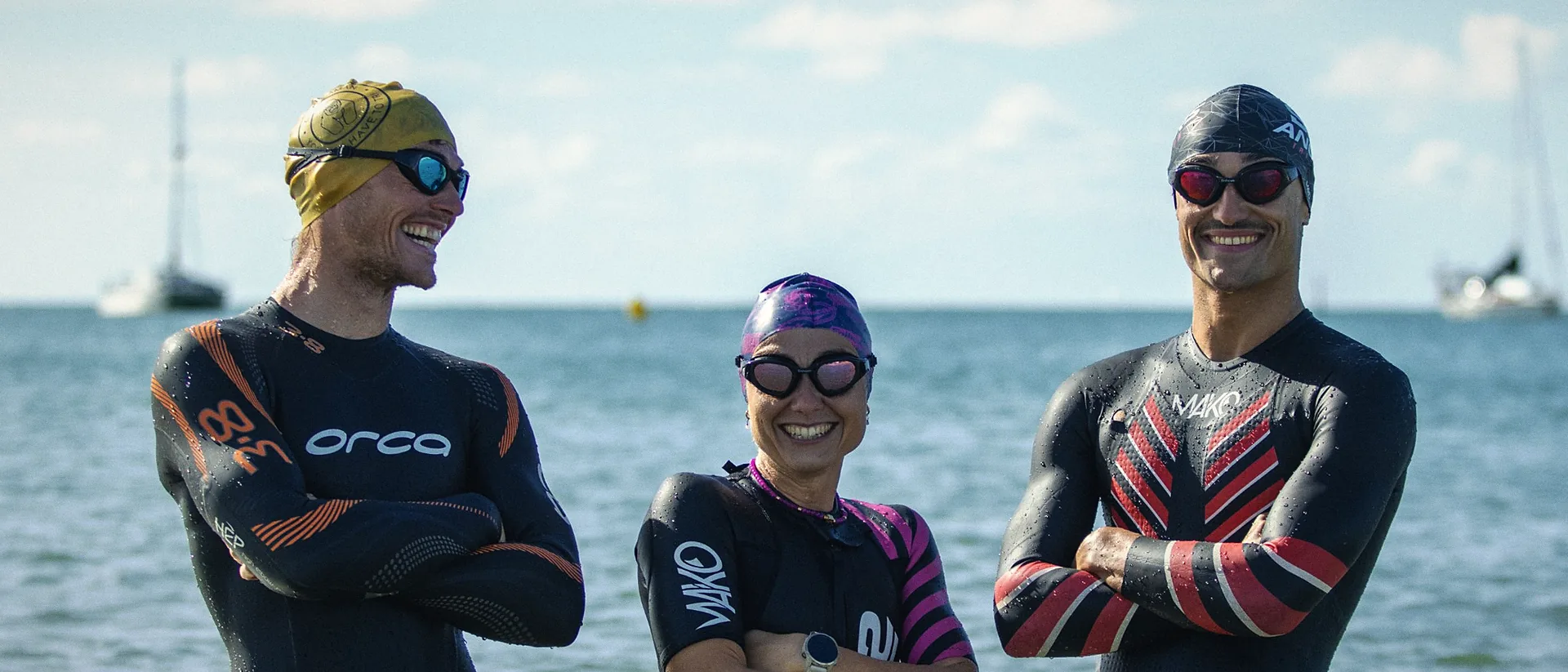 Trois triathlètes en combinaison, bras croisés, au bord de la mer