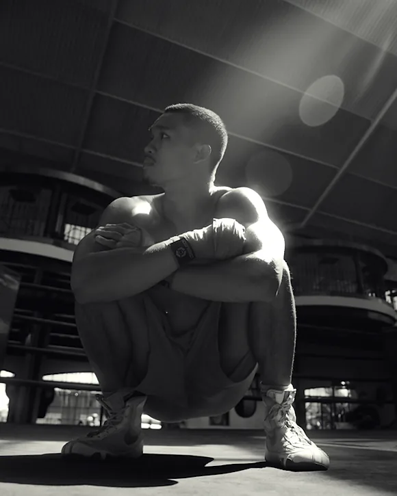 Boxeur accroupi sur le ring en contre-plongée, lumière du jour dans la charpente, en noir et blanc