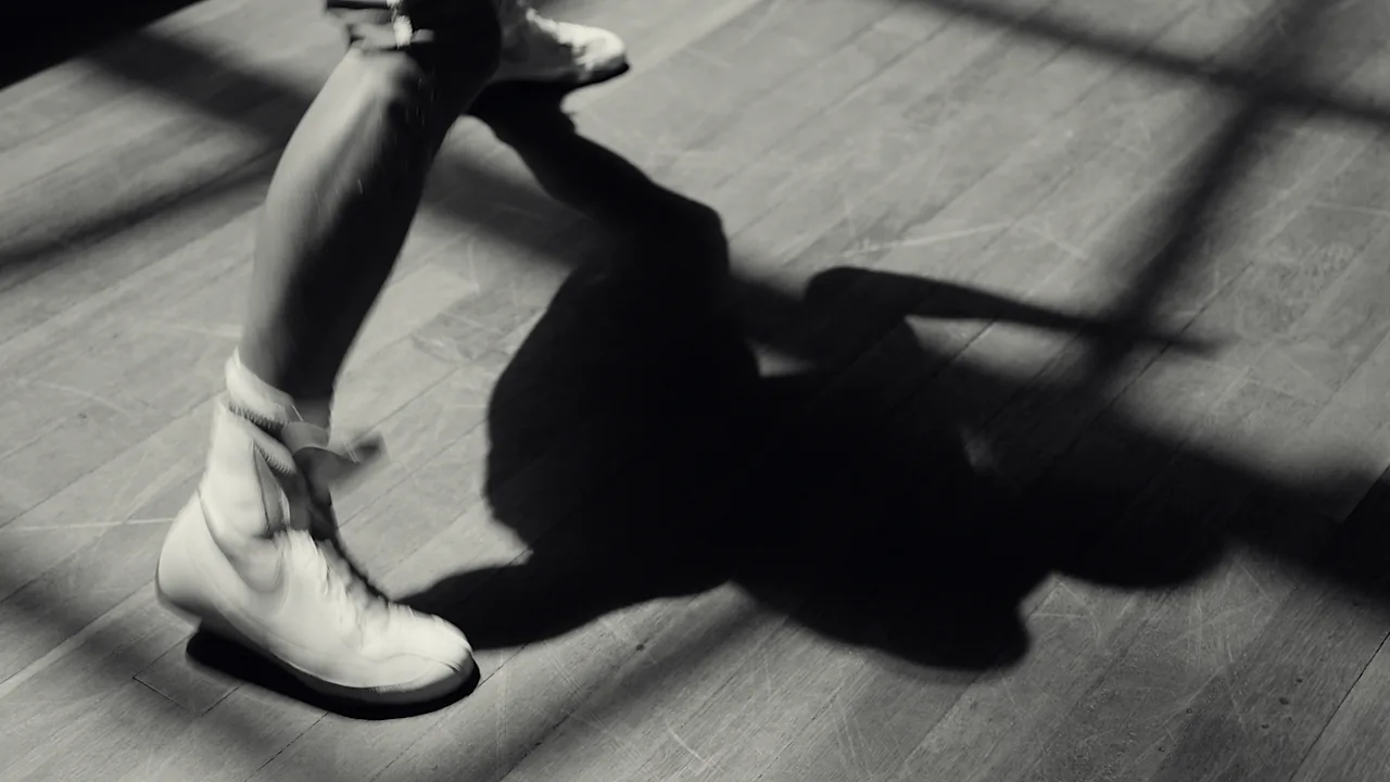 Chaussures de boxe et ombre d’un boxeur sur le parquet, en noir et blanc
